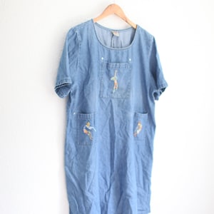 May include: A light blue denim dress with short sleeves and embroidered figures on the pockets.
