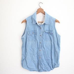 May include: A light blue denim sleeveless shirt with a button-up front and two chest pockets.