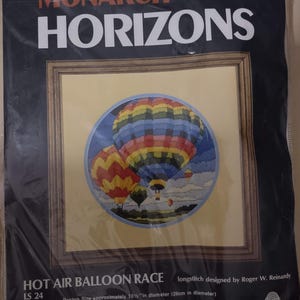 May include: A cross-stitch kit featuring a colorful hot air balloon race design. The kit includes 100% Persian wool yarn, 12-mesh cotton canvas, a needle, and instructions. The design is approximately 10 inches in diameter.