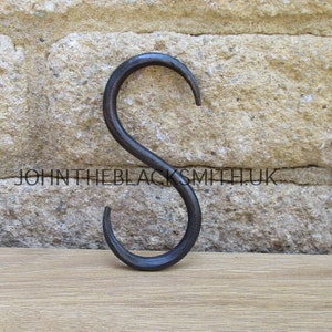 Può includere: Un gancio a forma di S in metallo nero. Il gancio è in ferro battuto e ha una finitura rustica.