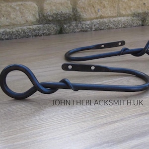 Un par de sujetadores de cortina de hierro forjado con remates en forma de cola de ratón forjados.