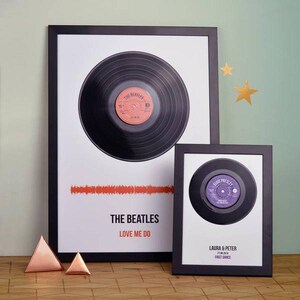 Two black vinyl record framed song prints showing personalised labels, a red sound wave and the text “THE BEATLES”, “LOVE ME DO”, “LAURA & PETER”, “21.02.2014” and “FIRST DANCE”.