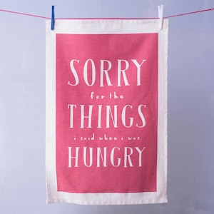 May include: A pink tea towel with the text "SORRY for the THINGS I said when I was HUNGRY" in white.