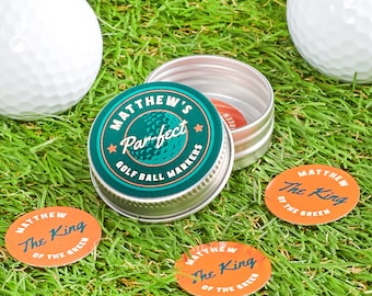 May include: A set of golf ball markers in a small metal container. The container is labeled "Matthew's Par-fect Golf Ball Markers". The markers are round and orange with the text "Matthew The King of the Green" printed on them.