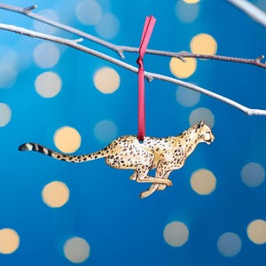 May include: A wooden cheetah ornament with a red ribbon hanging from a branch. The cheetah is painted in realistic colours and is running.