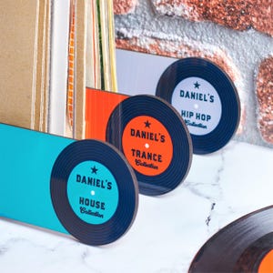Puede incluir: Tres separadores en forma de disco de vinilo negro con texto blanco y naranja. El texto dice "Daniel's House Collection", "Daniel's Trance Collection" y "Daniel's Hip Hop Collection".