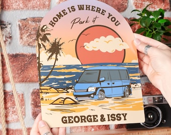 May include: A retro-style illustration of a blue van parked on a beach at sunset. The text reads "Home is where you park it" and "George & Issy".