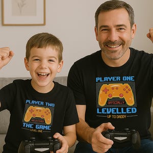 Pode incluir: Duas pessoas vestindo camisetas pretas com tema de videogame. O texto nas camisetas diz "Player One Officially Levelled Up To Daddy" e "Player Two Has Entered The Game Level One".