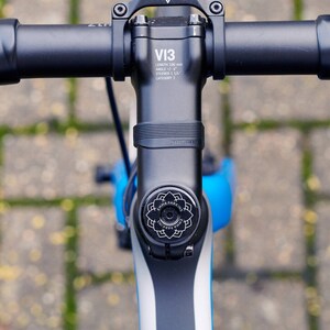 Top view of a black bike headset cap engraved with “EMMA PARKINS” in a floral mandala design, fitted centrally to the stem of a blue bicycle.