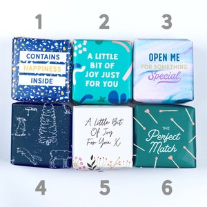 Puede incluir: Seis peque&ntilde;as cajas de regalo con diferentes dise&ntilde;os y textos. Las cajas est&aacute;n dispuestas en dos filas de tres. La fila superior tiene una caja azul con el texto "Contiene felicidad dentro", una caja turquesa con el texto "Un poco de alegr&iacute;a solo para ti", y una caja morada con el texto "&Aacute;breme para algo especial". La fila inferior tiene una caja azul con un dise&ntilde;o de &aacute;rbol y ciervo, una caja blanca con el texto "Un poco de alegr&iacute;a para ti X", y una caja verde con el texto "La pareja perfecta".