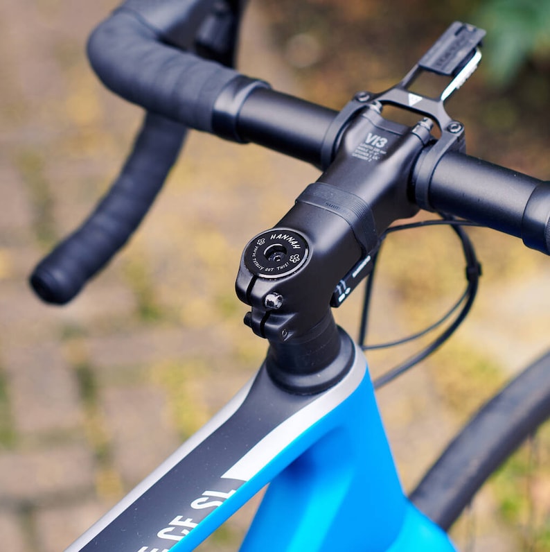 Black personalised bicycle headset cap fitted to a road bike, engraved with the name “HANNAH” and the message “YOU’VE TOTALLY GOT THIS!” with flower motifs.