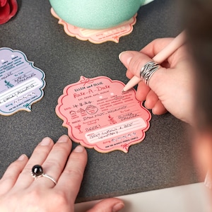 May include: A pink and white card with the text "Ellen and Ollie Rate-A-Date" and a checklist for rating a date. The checklist includes categories like "Eat, Drink, Rate, Repeat", "Breakfast", "Lunch", "Dinner", "Drinks", "Home Cooked", "Take Away", "Trees", "Meal Out", "Tags", "Other", "Where", "Accompanying", "The Dish", "Butter Pancer", "Notes", and "Best Curry & Best Company".
