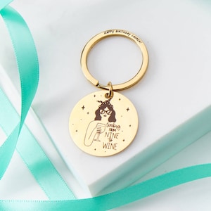May include: A gold-coloured keyring with a circular pendant. The pendant has an illustration of a woman with a wine glass and the text "Working from Nine to Wine". The words "Happy Birthday Lauren!" are also engraved on the keyring.