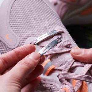 K&ouml;nnte beinhalten: Rosa Laufschuhe mit orangefarbenen Akzenten und silbernen Schnallenschmuck, auf denen "Keep Going Mumi" und "You Can Do It" steht.