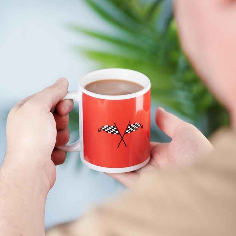 Puede incluir: Una taza de cer&aacute;mica roja con asa blanca y un dise&ntilde;o de bandera a cuadros. La taza est&aacute; llena de un l&iacute;quido marr&oacute;n.