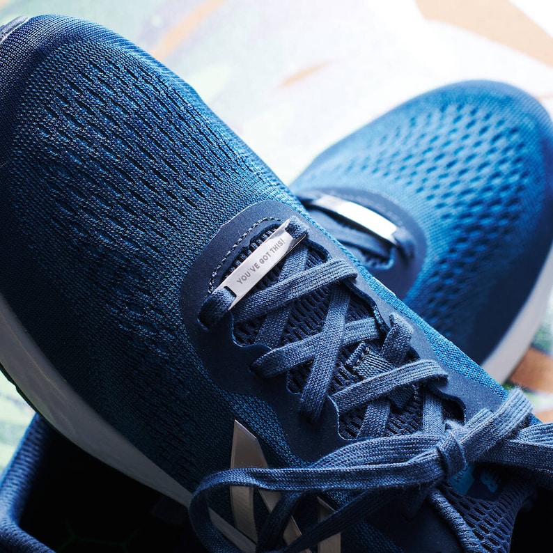 K&ouml;nnte beinhalten: Blaue Laufschuhe mit einem silbernen Schnallenanh&auml;nger mit der Aufschrift "You've got this".