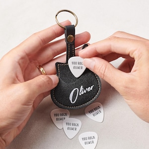 Può includere: Portachiavi nero in pelle a forma di plettro per chitarra con il nome "Oliver" e plettri bianchi con la scritta "YOU ROCK OLIVER". Il portachiavi ha un anello di metallo e un design cucito.