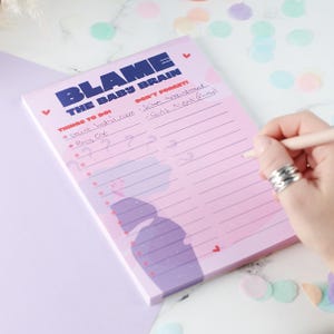 May include: Pink notepad with the text "Blame the Baby Brain" and a list of things to do and don't forget items. The list includes "Paint baby's room", "Buy cot", "Scan appointment", and "Girls Night (Friday)".