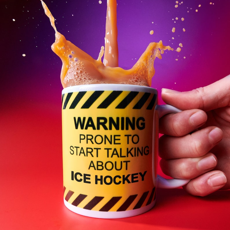 Yellow personalised ice hockey mug with black hazard stripes, held by a hand beside a splash of orange drink. Text reads “WARNING PRONE TO START TALKING ABOUT ICE HOCKEY”.