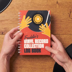 May include: A red spiral-bound log book titled "Freddie's Vinyl Record Collection Log Book." The cover features a graphic of a vinyl record with yellow hands and the text "For Serious Vinyl Collectors."