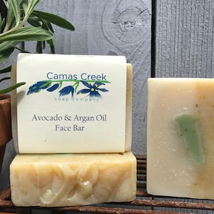 May include: Two bars of handmade soap, one with a label that reads "Camas Creek Soap Company Avocado & Argan Oil Face Bar", and the other with a green swirl.