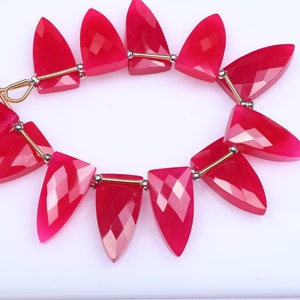 May include: A strand of bright pink gemstone beads, each bead is faceted and shaped like a teardrop. The beads are strung on a gold wire with silver spacers.