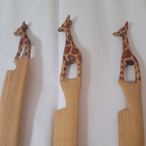 May include: Three wooden giraffe bookmarks with brown and tan spots. The giraffes are carved in a standing position with their necks arched.
