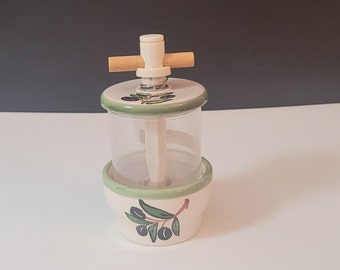 May include: White ceramic olive oil dispenser with a green olive branch design. The dispenser has a clear glass container and a wooden handle.