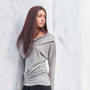 May include: A woman wearing a gray long-sleeved shirt with a cowl neck and black pants.