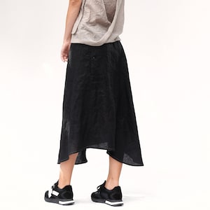 May include: A woman wearing a light brown sleeveless top with a criss-cross back detail and a black midi skirt. She is wearing black and white trainers.
