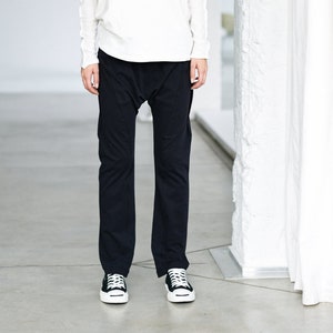 May include: A woman wearing a white, loose-fitting, long-sleeved shirt with a high neckline and black, loose-fitting pants. She is wearing black and white sneakers.