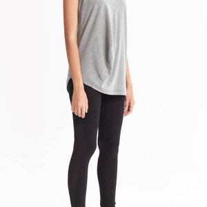 May include: A woman is wearing a gray sleeveless top with a cowl neck and black leggings.