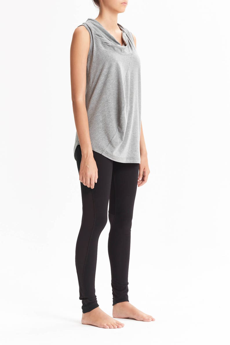 May include: A woman is wearing a gray sleeveless top with a cowl neck and black leggings.