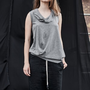 May include: A gray sleeveless top with a cowl neck and a black pair of pants with a drawstring.