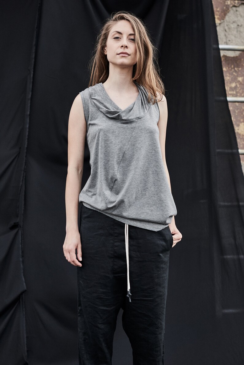 May include: A gray sleeveless top with a cowl neck and a black pair of pants with a drawstring.