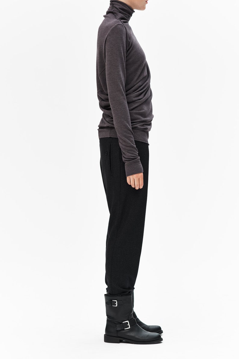 Puede incluir: Un jersey de cuello alto gris oscuro con mangas largas y silueta ajustada. El jersey se combina con pantalones negros y botines negros.