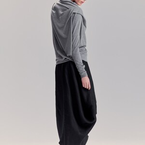 May include: A woman wearing a gray long-sleeved shirt with a draped neckline and a black, flowing skirt. She is wearing black shoes.