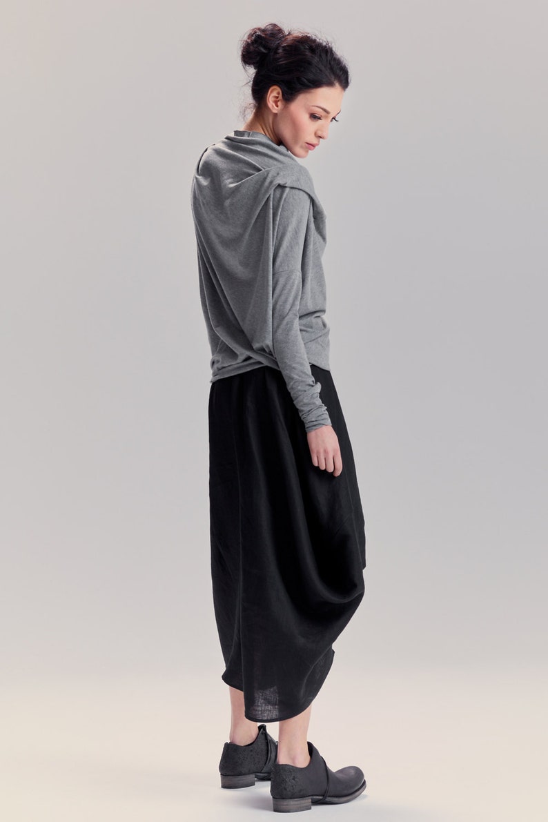 May include: A woman wearing a gray long-sleeved shirt with a draped neckline and a black, flowing skirt. She is wearing black shoes.