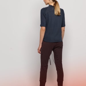 May include: A woman wearing a dark blue short-sleeved shirt and dark brown pants. She is wearing black sandals and has her hair pulled back in a ponytail.