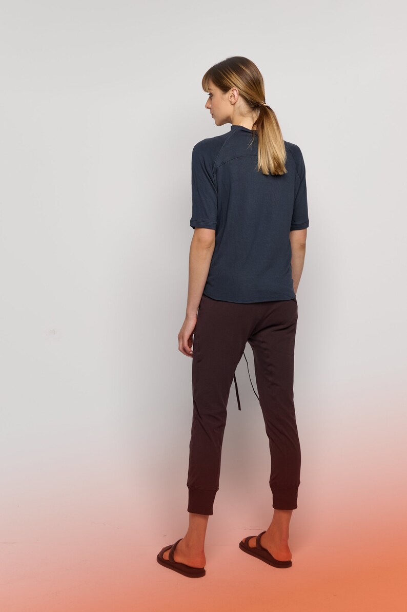 May include: A woman wearing a dark blue short-sleeved shirt and dark brown pants. She is wearing black sandals and has her hair pulled back in a ponytail.