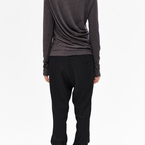Puede incluir: Una camisa gris carb&oacute;n de manga larga con cuello alto y dise&ntilde;o drapeado. La camisa se combina con pantalones negros y botines negros de tobillo.