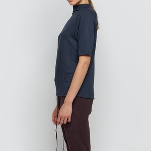 May include: A woman wearing a dark blue mock neck shirt with short sleeves and brown pants.