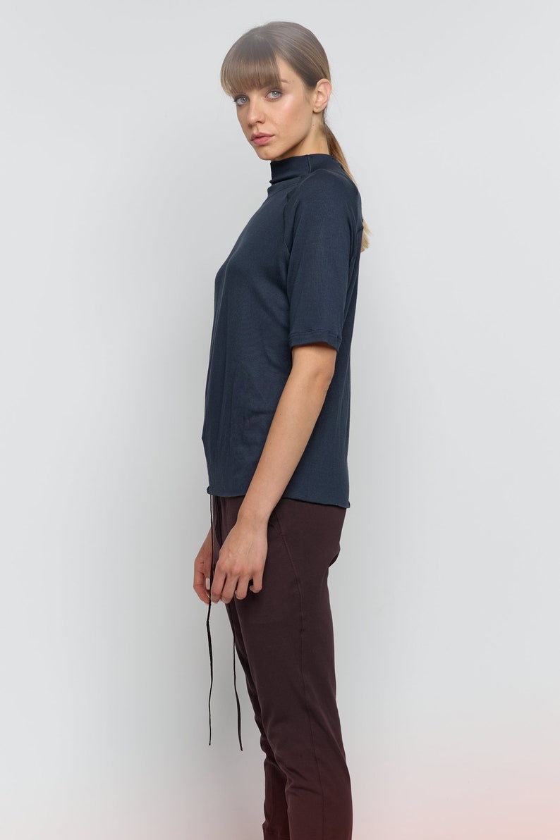 May include: A woman wearing a dark blue mock neck shirt with short sleeves and brown pants.