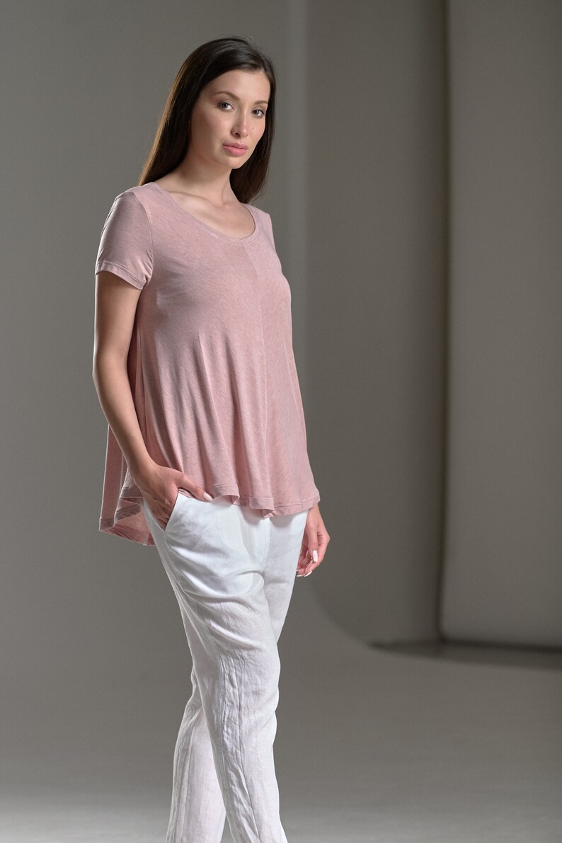 Puede incluir: Una mujer con una camiseta de manga corta de color rosa claro y holgada y pantalones de lino blancos.