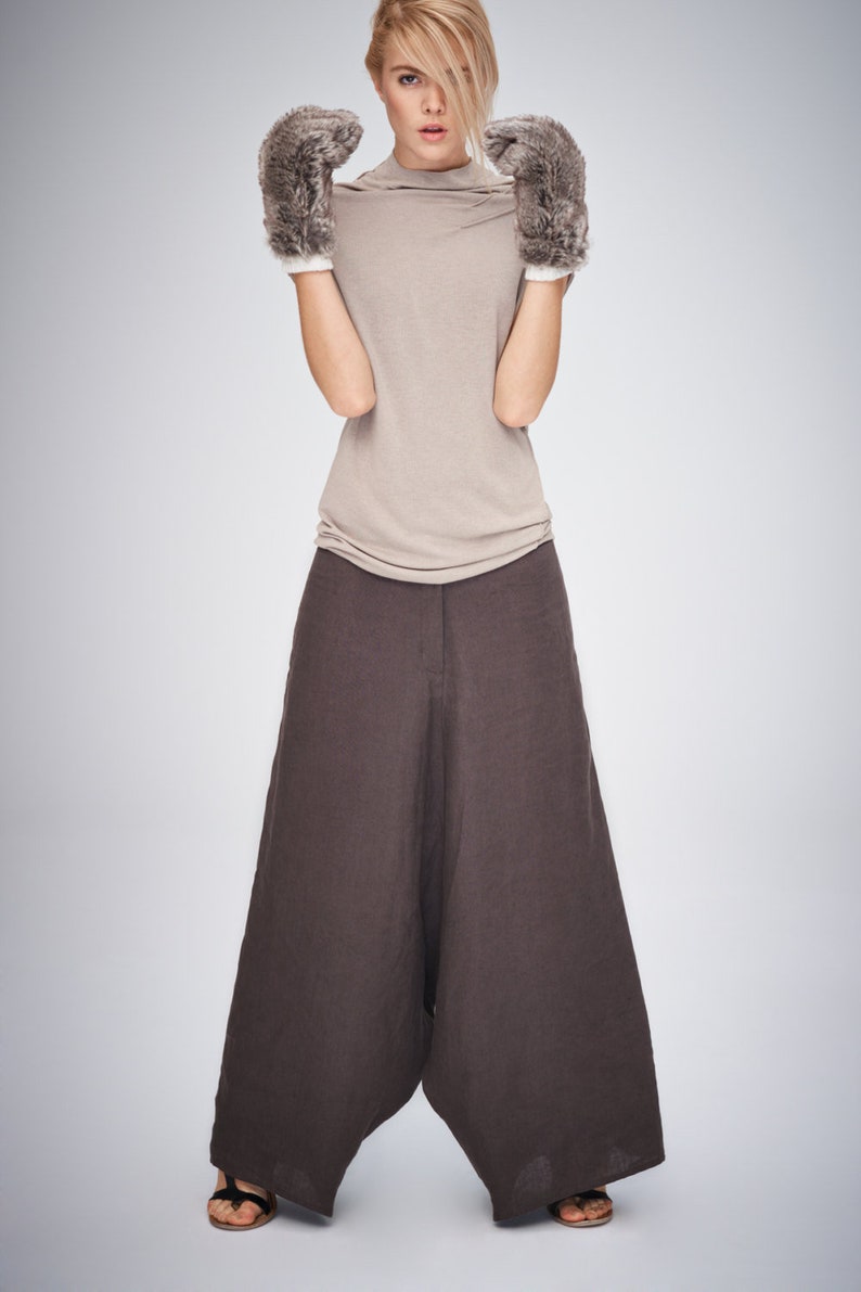 May include: A woman wearing a beige turtleneck top, wide-leg brown pants, and furry gray gloves with white cuffs. The outfit is simple and modern, suitable for fall or winter wear.