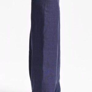 May include: A pair of loose-fitting, dark navy blue trousers with a visible woven texture, featuring a simple elasticized waistband and a straight-leg cut that extends to the floor, paired with a plain, light beige short-sleeved t-shirt.