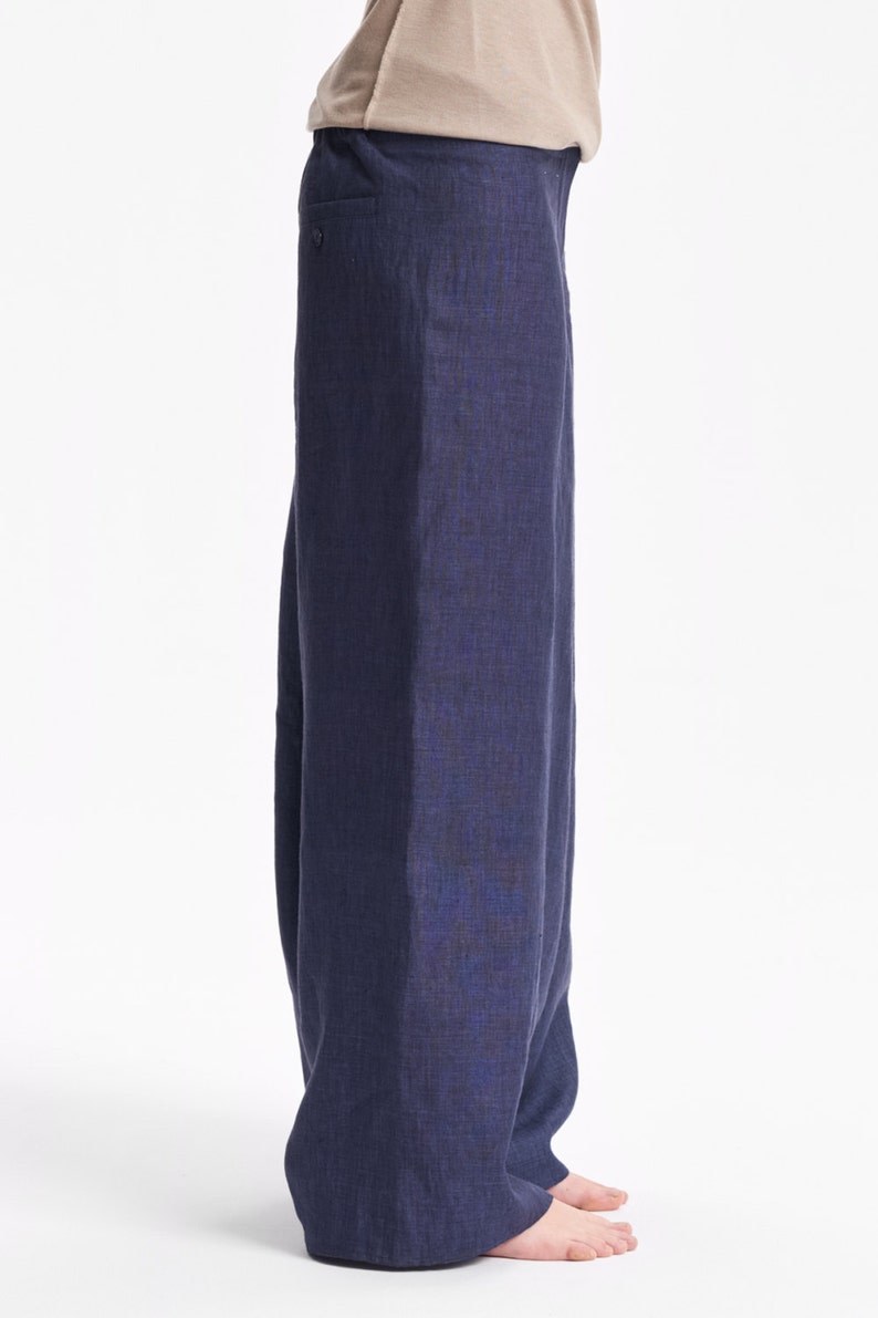 May include: A pair of loose-fitting, dark navy blue trousers with a visible woven texture, featuring a simple elasticized waistband and a straight-leg cut that extends to the floor, paired with a plain, light beige short-sleeved t-shirt.