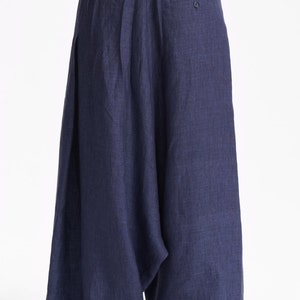 May include: Wide-leg navy blue trousers with a loose, flowing silhouette and a gathered elastic waistband. The pants feature a visible single button detail on the upper right side and a textured fabric finish, paired with a plain beige short-sleeve top.