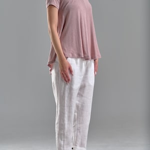 Puede incluir: Una mujer con una camiseta de manga corta rosa polvoriento y pantalones de lino blancos con sandalias negras.