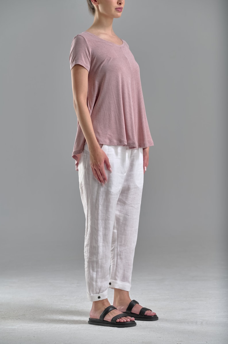 Puede incluir: Una mujer con una camiseta de manga corta rosa polvoriento y pantalones de lino blancos con sandalias negras.
